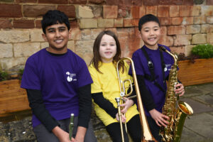 3 young musicians smiling holding instruments