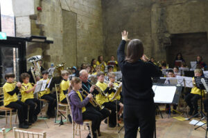 Young musicians sat with instruments, conductor stood in front.