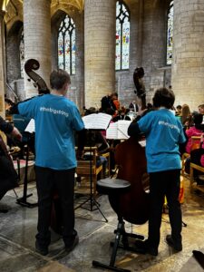 2 young male double bass players stood up in blue tshirts